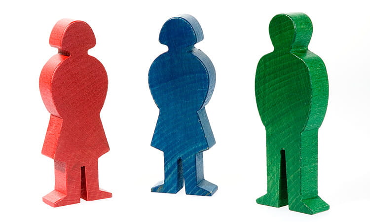 Three wooden figures stand upright: one red, one blue, and one green, each with simplified, stylized human shapes.