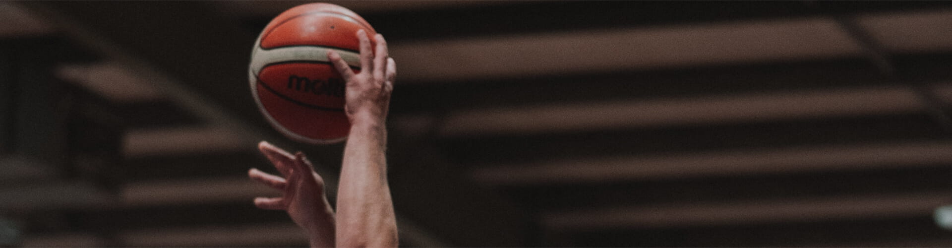 A person is reaching up to grab a basketball with both hands against a blurred indoor background.