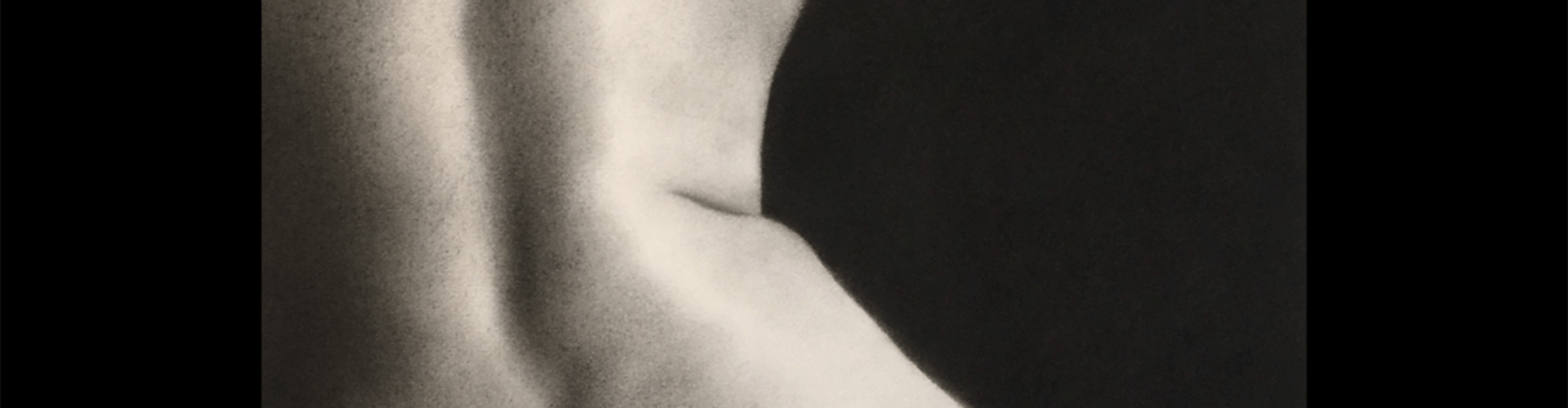 A monochrome image focused on the curved lines of a person's back, highlighting the shoulder and upper arm against a dark background.