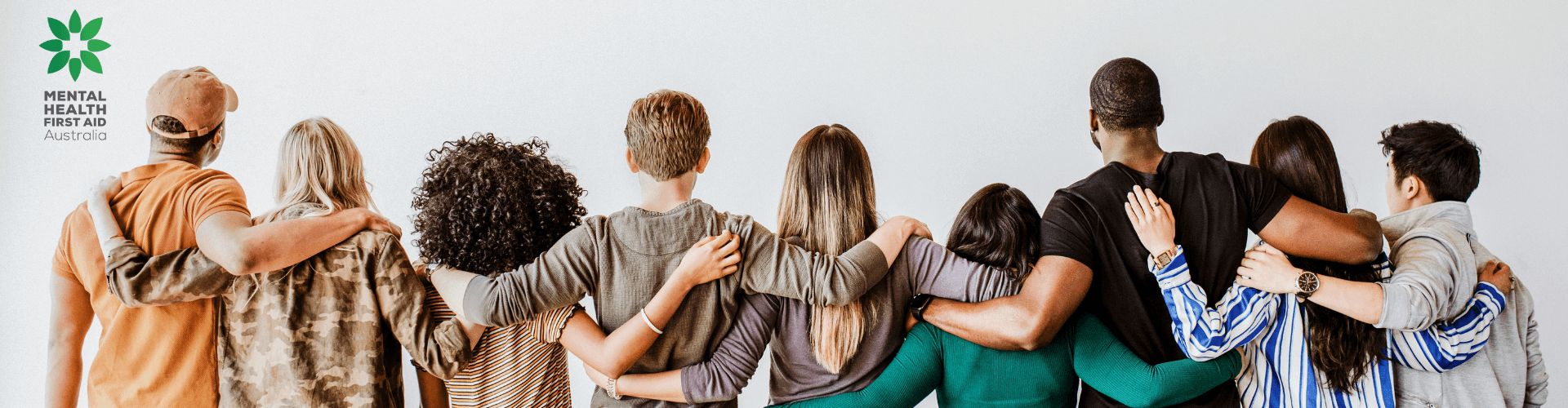 A diverse group of people with arms around each other’s backs stand facing away from the camera; Mental Health First Aid Australia logo is visible on the left.