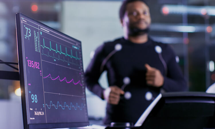 A man wearing sensors jogs on a treadmill while a monitor displays his heart rate, blood pressure, and ECG data.