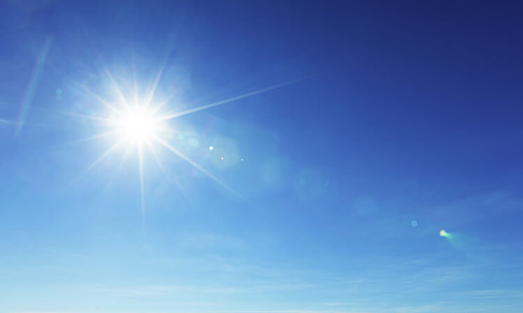 Bright sun shining in a clear blue sky with lens flare effects and a faint gradient near the horizon.