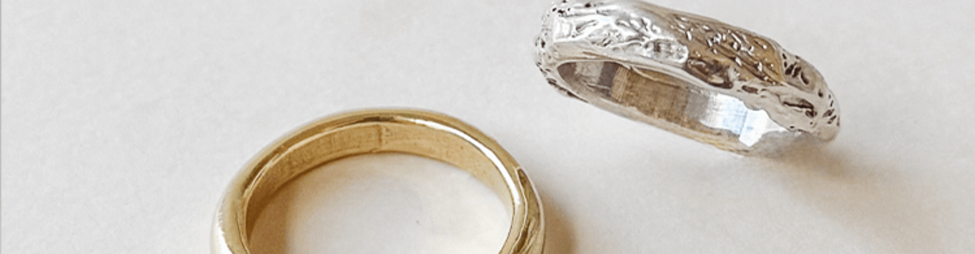 A plain gold ring and an ornate silver ring are placed side by side on a white surface.