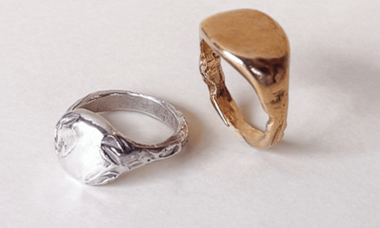 Two worn signet rings, one silver-colored and one gold-colored, are placed on a white surface.