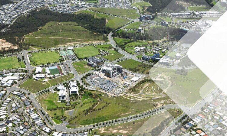 Aerial view of a suburban area with houses, roads, green fields, and several large buildings at the center.