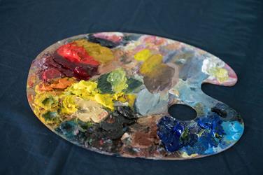 A wooden artist’s palette with various colors of oil paint arranged and mixed, resting on a dark blue surface.