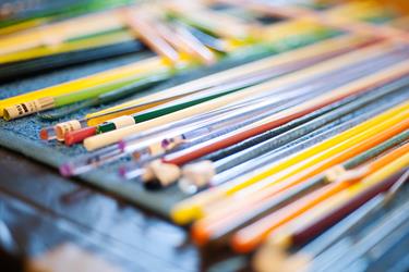A close-up view of colored glass rods and glassblowing tools arranged on a blue cloth, with a shallow depth of field.