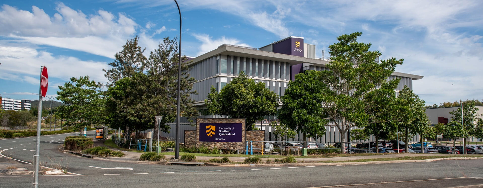 University of Southern Queensland Springfield campus building with a UniSQ logo visible, surrounded by trees and a parking lot.