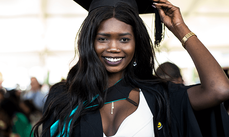 A smiling graduate adjusting her mortarboard.