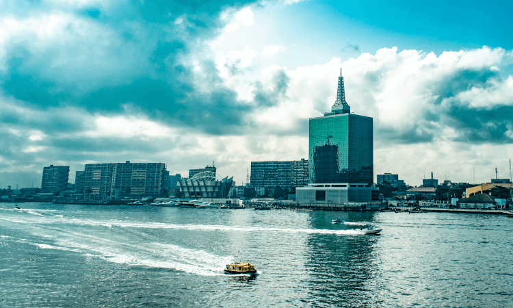 Cityscape of Lagos waterfront with high-rise buildings, a small boat on the water, and a partly cloudy sky overhead.