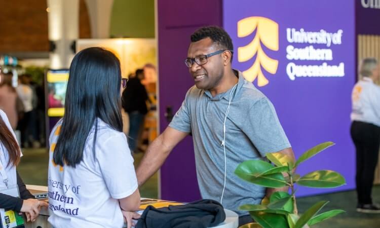Two individuals engaging in conversation at a UniSQ information booth.