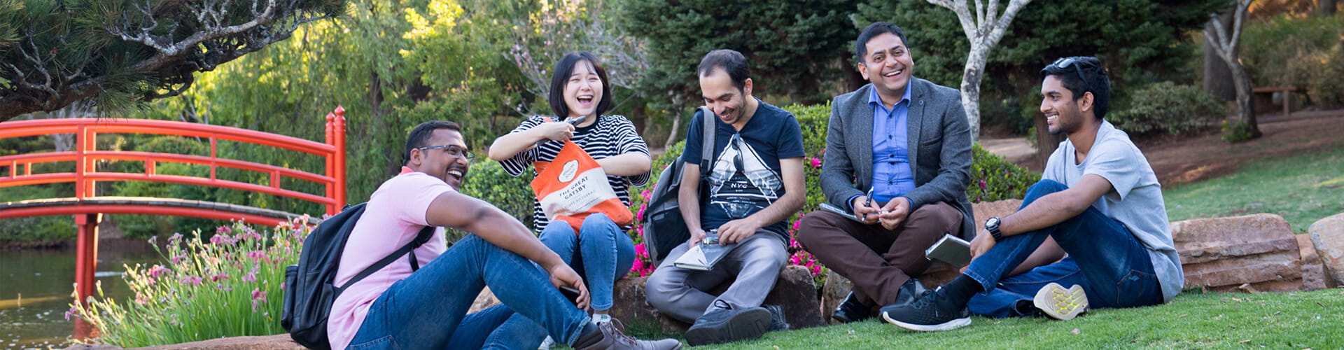 Group of friends enjoying a laughter-filled gathering at the Toowoomba Japanese Gardens with a red bridge in the background.