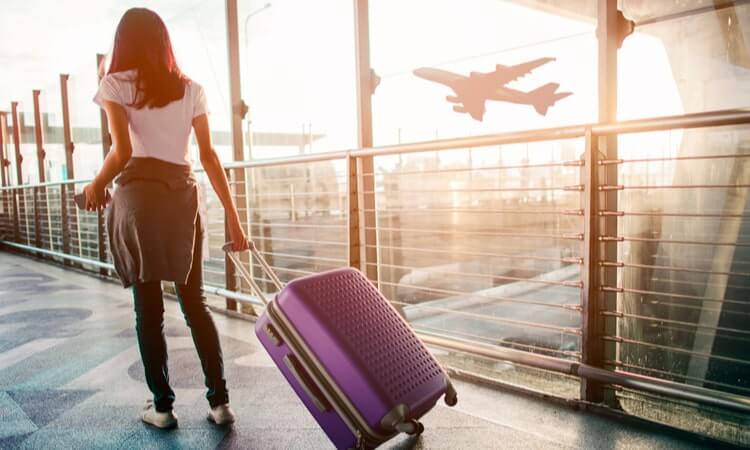 Woman with suitcase watching an airplane take off from airport terminal.