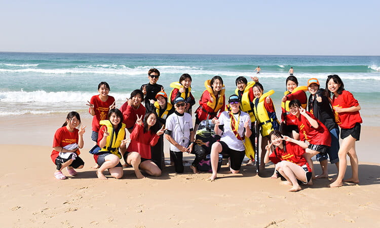 Group of people posing for a photo on a sandy beach with the ocean in the background.