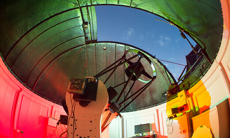 Interior of an observatory dome with a telescope pointing towards the open slit.