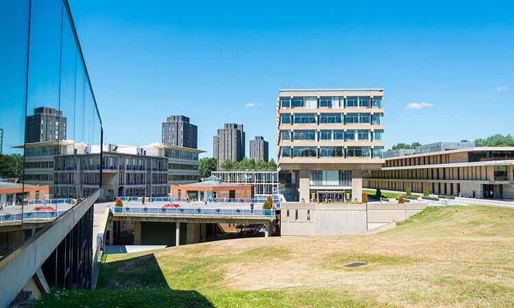Modern university campus with contemporary architecture and students milling about on a sunny day.