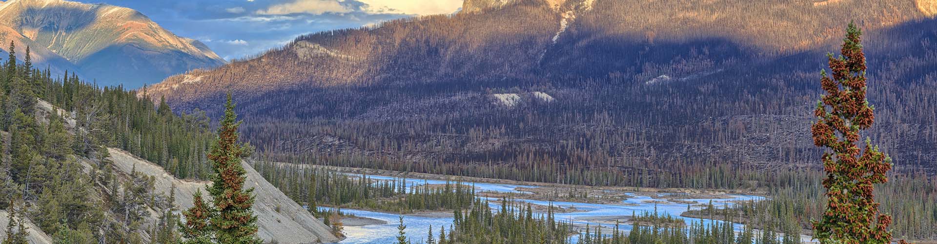 A panoramic view of a river flowing through a mountainous landscape at sunset.