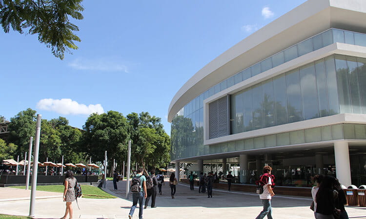 Students walking outside a modern university building on a sunny day.