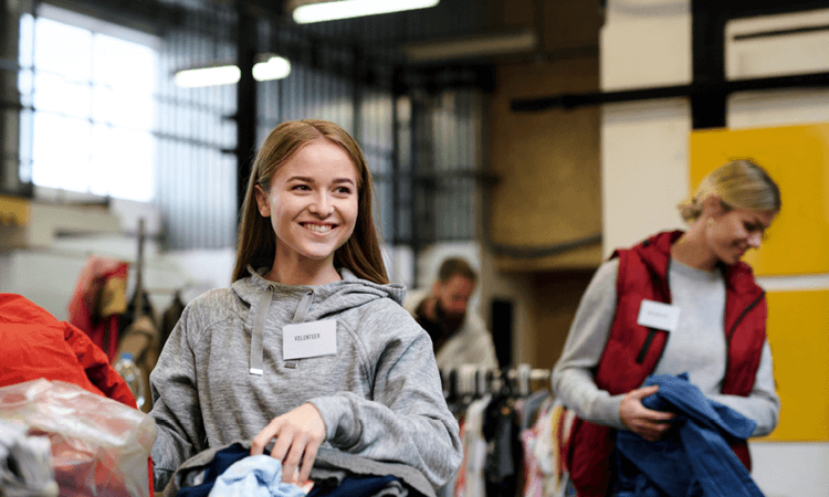 A smiling volunteer sorting clothes at a donation center with other workers in the background.