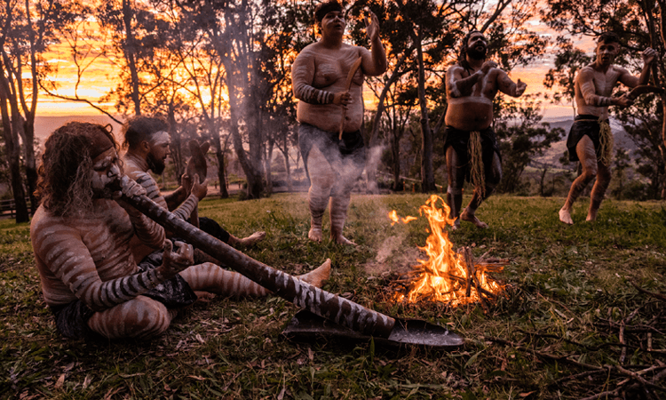 Group of indigenous people performing a traditional dance around a fire at sunset.