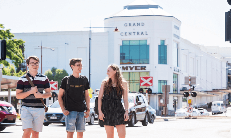 Three people walking across a street with a shopping center in the background.