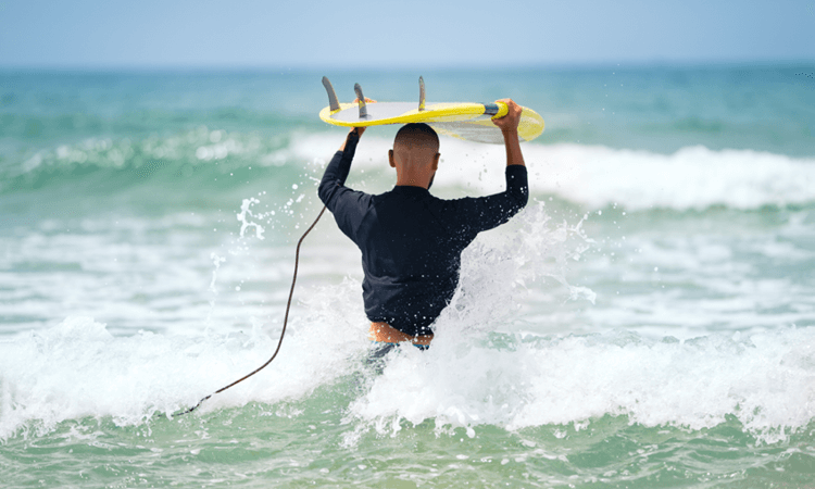 Surfer with a yellow board navigating through shallow waves at the beach.