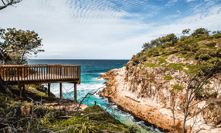 Wooden viewing platform overlooking a rocky cove with clear turquoise waters.