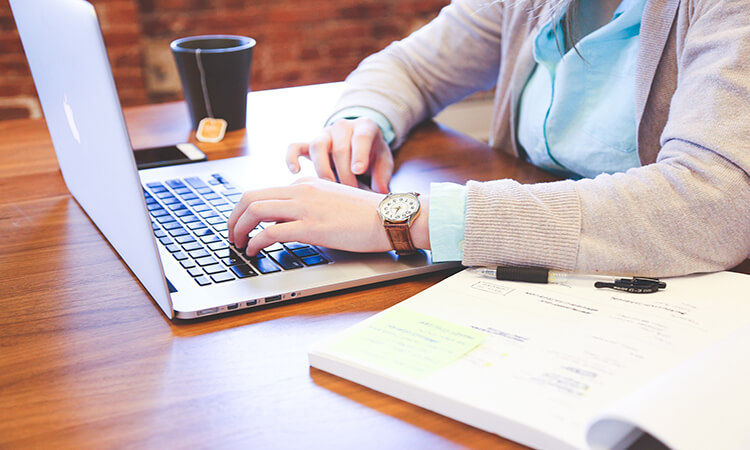 Cropped image of student working at laptop with an open notebook and tea beside her