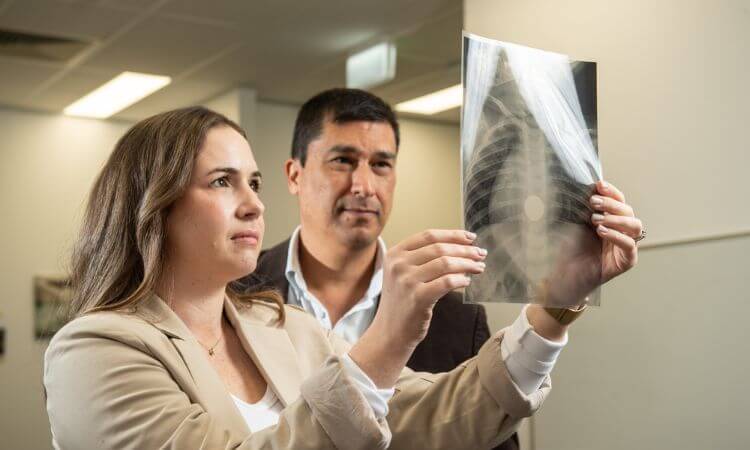 A man and woman look at an x-ray image held up to the light. A button is visible in the image.