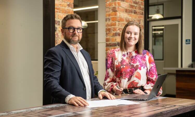 Two people sitting at a desk, smiling at the camera.