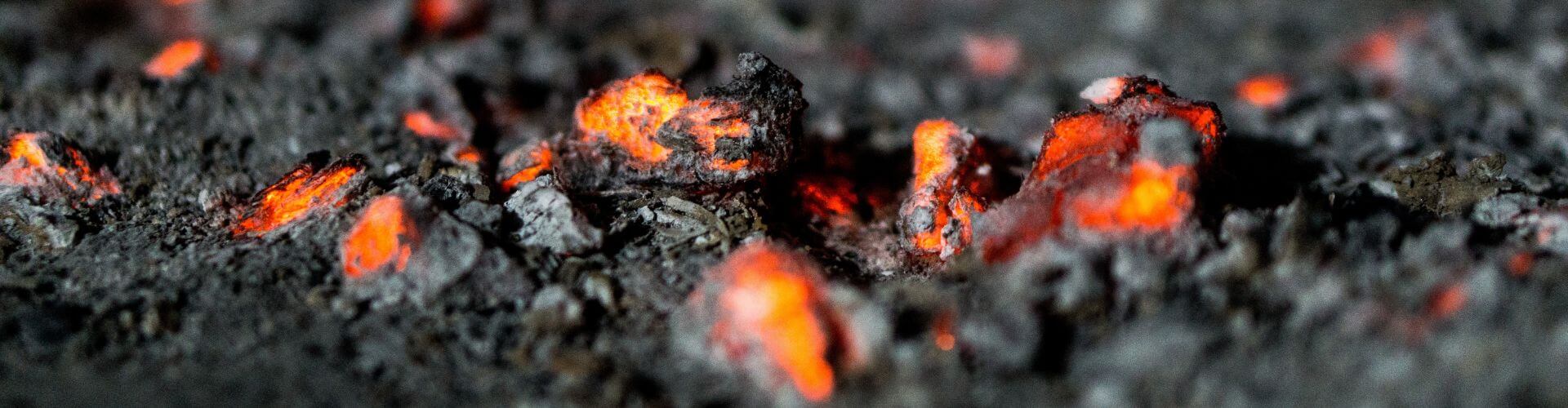 A close-up image of burning embers and ash on the ground. 