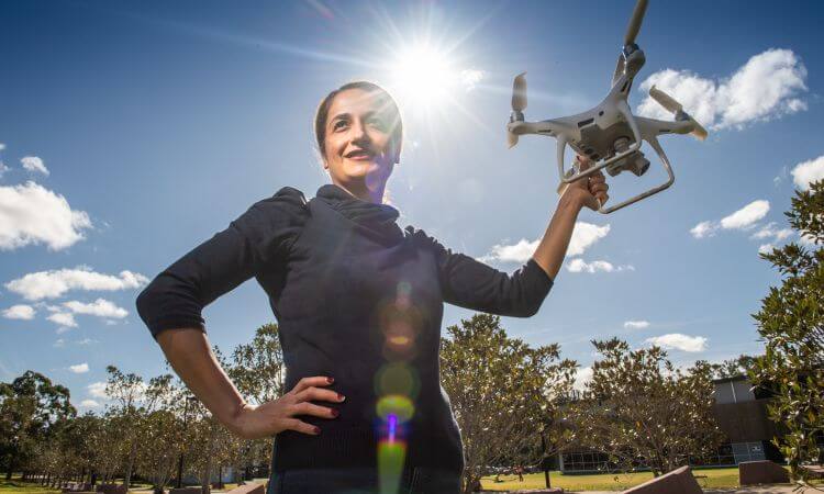 Associate Professor Zahra Gharineiat stands smiling with one hand on her hip and the other hand holding a white drone.