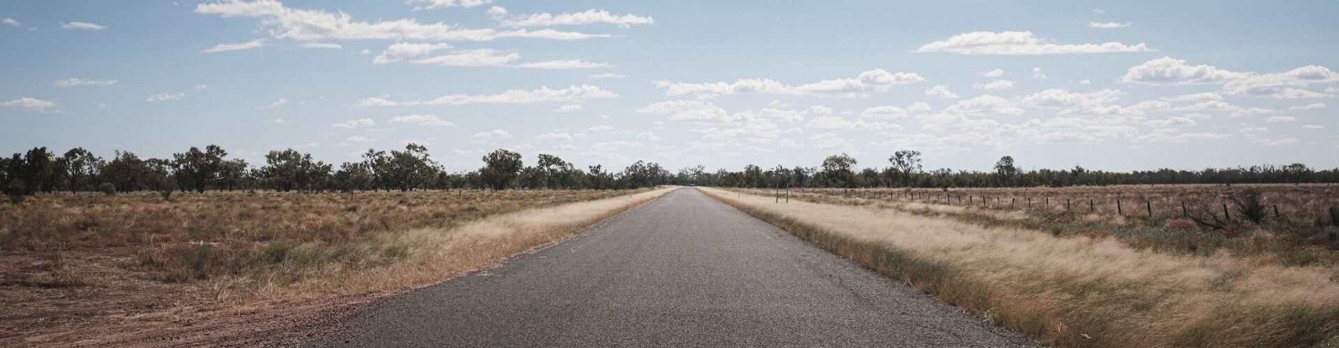 A bitumen road cuts through the middle of dry, rural land. The blue sky is bright and clear.