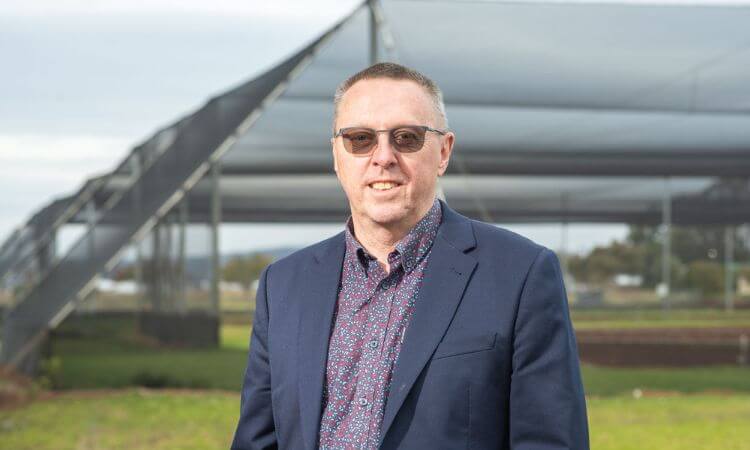 man in glasses standing in front of glasshouses