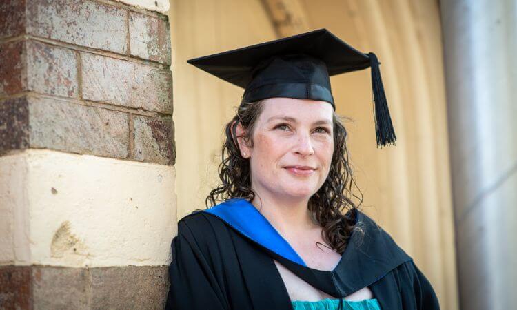 lady in graduate gown smiling on brick wall 