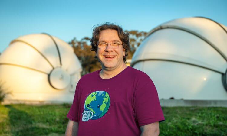 man in purple shirt smiling in front of telescopes