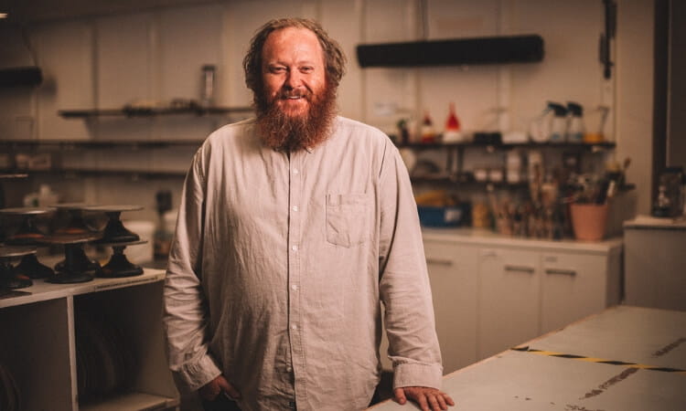 Bearded man in a casual shirt standing in an art room. 