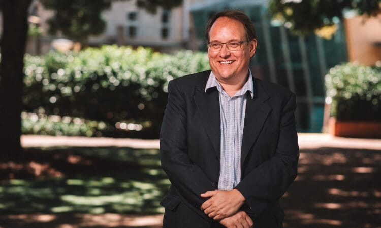 A man wearing glasses and a suit standing in a park.