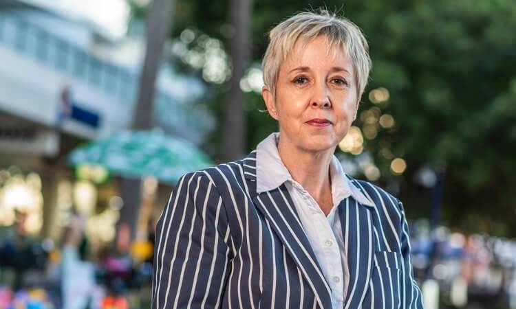 A woman with short hair wearing a striped blazer and a light shirt, standing outdoors.