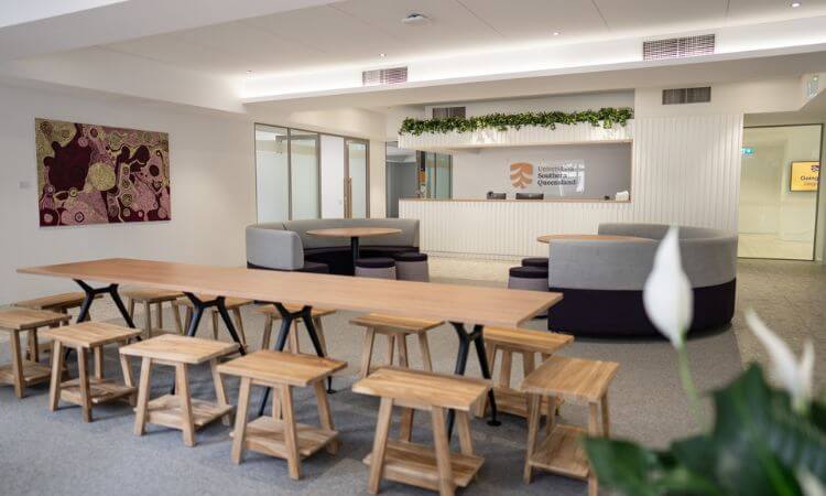 Modern office lobby with a reception desk, seating area, and wooden stools.