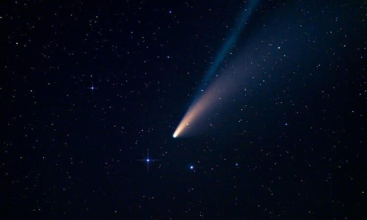A bright comet with a pronounced tail traveling through a starry night sky.