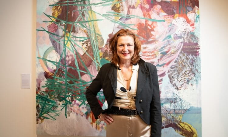 A woman standing in front of a colorful abstract painting in an art gallery, smiling at the camera.