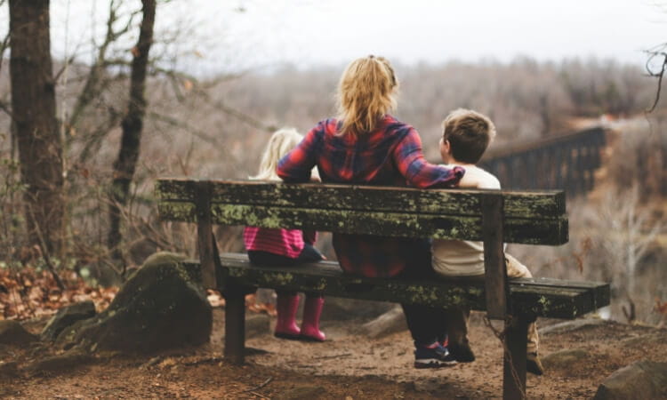 A person sits on a wooden bench with two children.