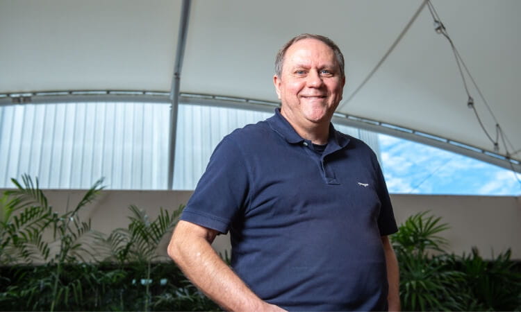 A man wearing a navy blue polo shirt stands and smiles inside a structure with a high, curved ceiling. 