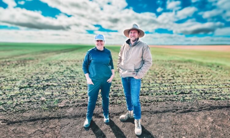 Two people stand in a farm field under a partly cloudy sky. 