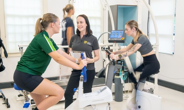 Two women are using exercise bikes in a gym.