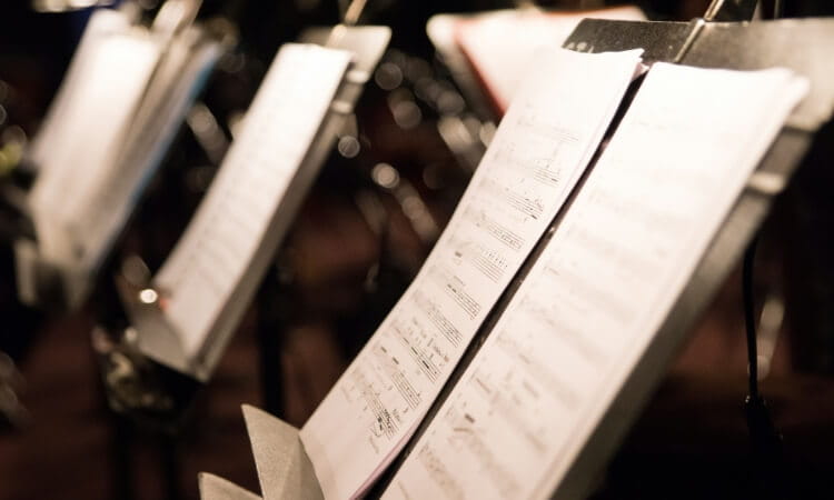 Close-up view of several music stands holding sheets of music in a dimly lit setting.