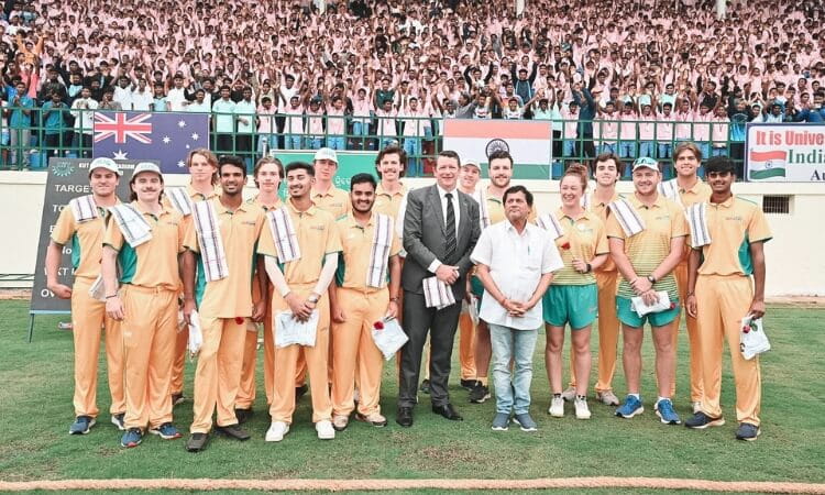 A cricket team in yellow uniforms stands on a field with several people in formal attire. 