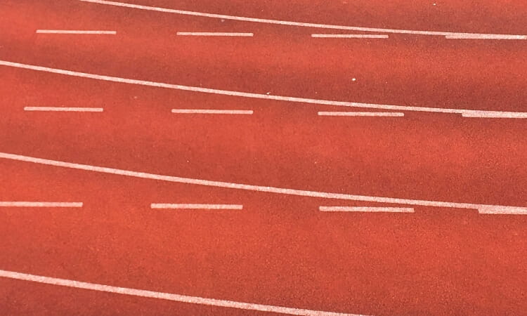 Close-up of curved running track lanes with dashed white lines on a red surface.