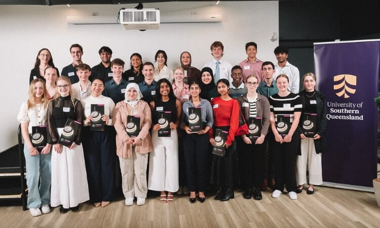 A group of young adults, holding awards, pose together in front of a University of Southern Queensland banner.